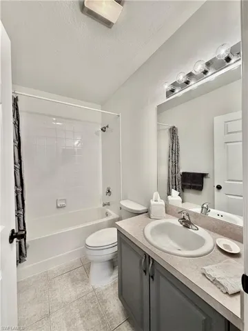 Bathroom with vanity, shower / bath combo, a textured ceiling, and light tile patterned flooring
