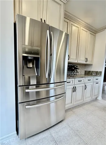 Kitchen with stainless steel fridge, dark stone counters, cream cabinets, and light tile patterned floors