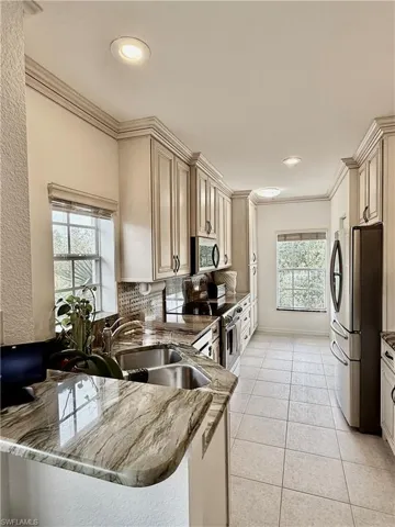 Kitchen featuring light stone countertops, stainless steel appliances, ornamental molding, decorative backsplash, and light tile patterned flooring
