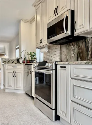 Kitchen with stainless steel appliances, light stone countertops, tasteful backsplash, light tile patterned floors, and cream cabinetry