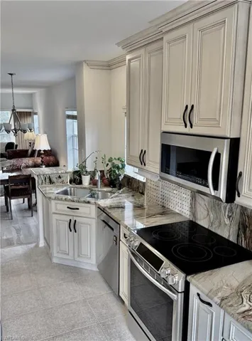 Kitchen with appliances with stainless steel finishes, a peninsula, light stone counters, and light tile patterned floors