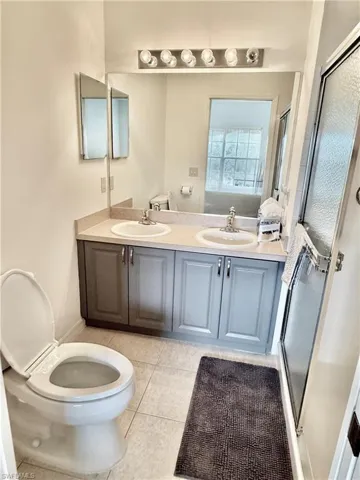 Bathroom with double vanity, a shower stall, and light tile patterned floors