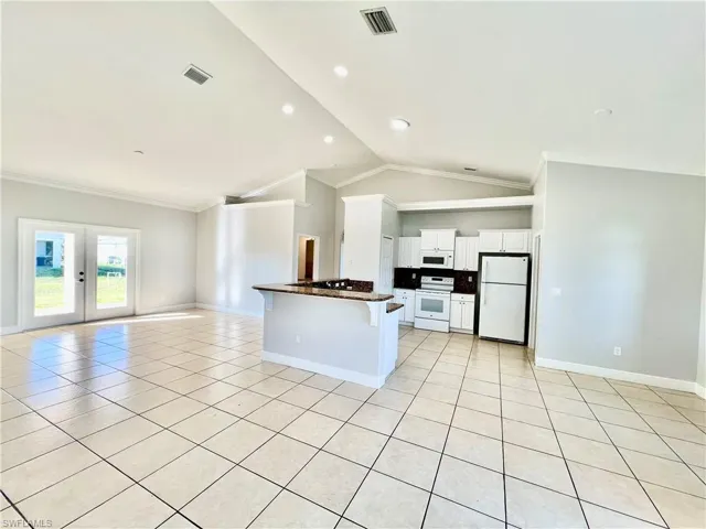 Kitchen with french doors, light tile patterned flooring, a kitchen breakfast bar, white appliances, and white cabinets
