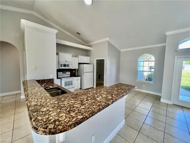 Kitchen with white cabinetry, white appliances, GRANITE TOPS, crown molding and a breakfast bar and pantry.