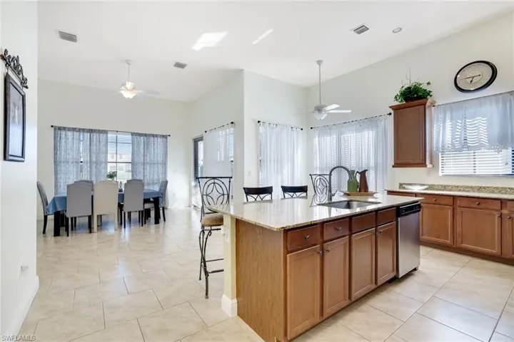 Kitchen with brown cabinets, a kitchen bar, light stone countertops, a kitchen island with sink, and light tile patterned floors