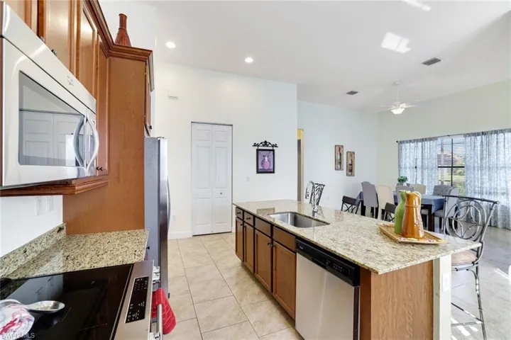 Kitchen featuring brown cabinetry, light stone counters, stainless steel appliances, light tile patterned flooring, and recessed lighting