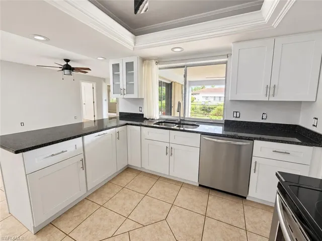 White cabinetry, dark stone countertops, stainless steel appliances, and a tile floor