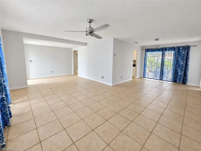 Expansive room with neutral tile flooring, a ceiling fan, and sliding glass doors