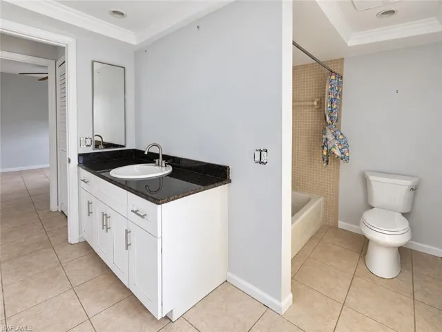 Tile flooring, white vanity with dark countertop, undermount sink, and shower/tub combination with tiled surround