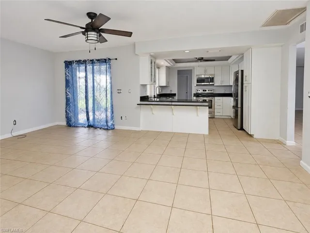 Tile flooring throughout, kitchen with white cabinetry, black countertops, stainless steel appliances, and a ceiling fan
