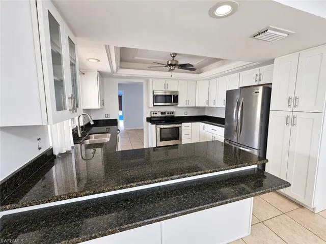 Kitchen featuring abundant white cabinetry, stainless steel appliances, dark stone countertops, a dual-basin sink, and recessed lighting