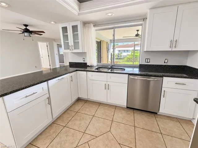 White cabinetry, dark stone countertops, stainless steel dishwasher, tile flooring, and a sliding glass door
