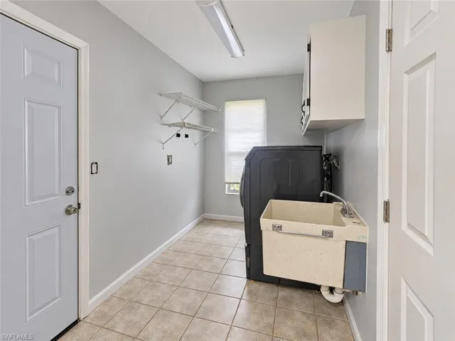 Tile flooring, utility sink with faucet, white wall cabinetry, and built-in shelving