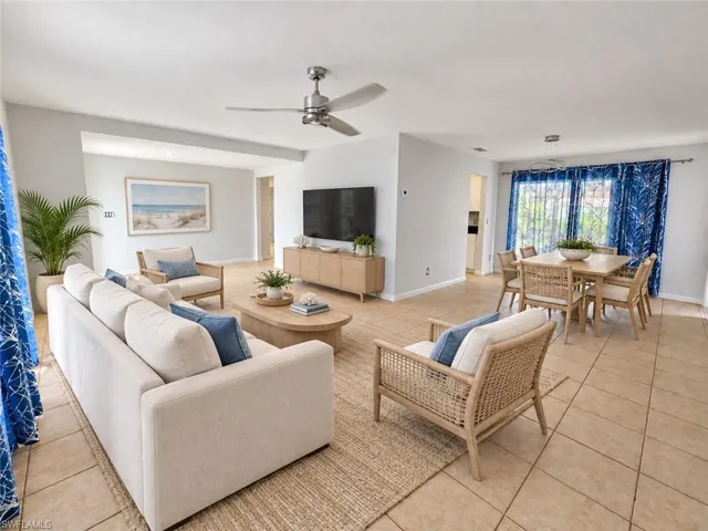 Expansive open-concept living and dining areas featuring large format tile flooring, a dining area with a linear chandelier, and a living area with a ceiling fan