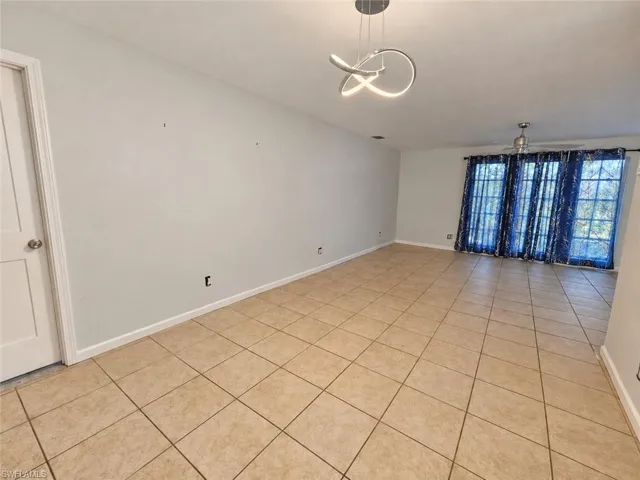 Expansive room featuring neutral-toned tile flooring, light-colored walls, a contemporary ceiling light fixture, and a ceiling fan
