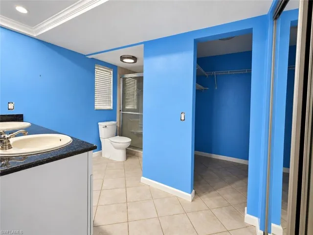 Dual vanity with undermount sinks, shower enclosure, built-in storage, closet with shelving, and tile flooring