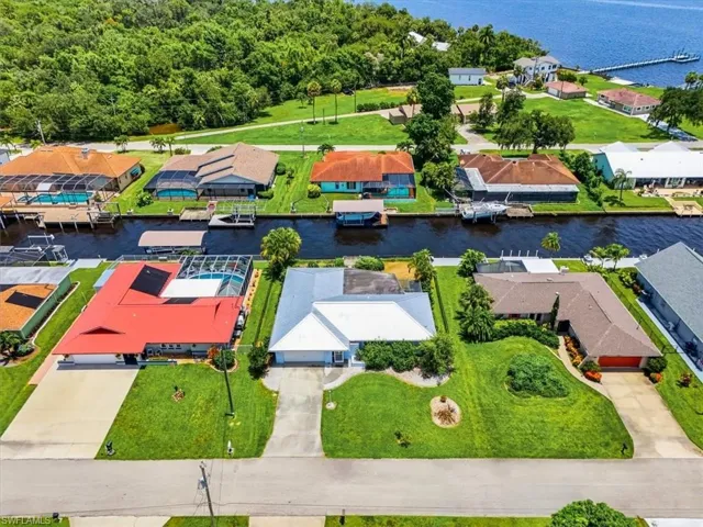 Canal-front property with a lush green lawn, mature trees, and an integrated garage