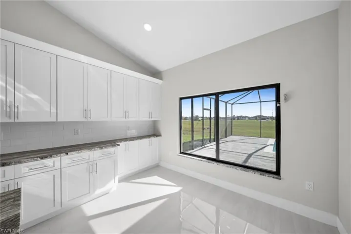 Kitchen featuring white cabinetry, lofted ceiling, dark stone counters, decorative backsplash, and recessed lighting