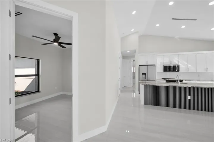 Kitchen featuring white cabinets, appliances with stainless steel finishes, high vaulted ceiling, light stone counters, and recessed lighting