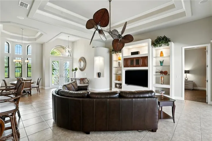 Living area featuring a raised ceiling, french doors, ornamental molding, light tile patterned floors, and a chandelier