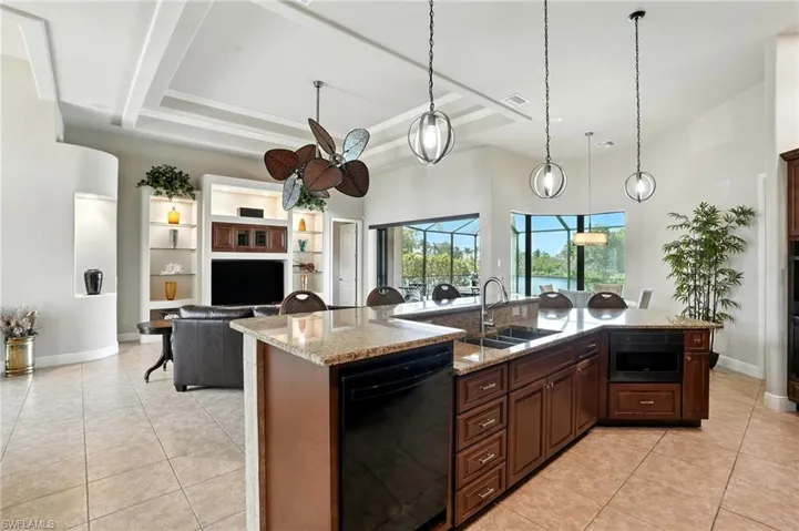 Kitchen featuring light stone countertops, dark brown cabinets, black dishwasher, decorative light fixtures, and a high ceiling