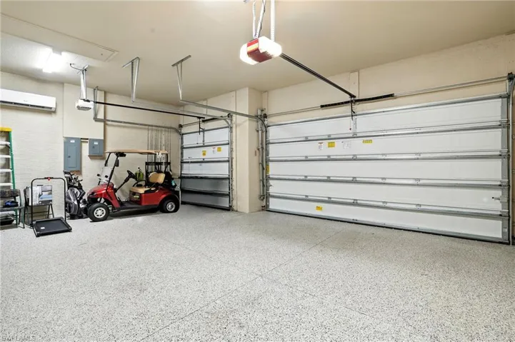 Garage with electric panel, a wall mounted air conditioner, and a garage door opener