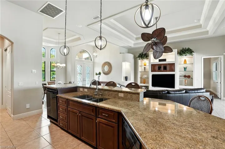 Kitchen with light tile patterned floors, pendant lighting, light stone counters, a tray ceiling, and open floor plan