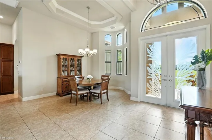 Dining room featuring french doors, a towering ceiling, light tile patterned floors, a raised ceiling, and a chandelier