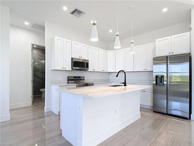 Kitchen featuring appliances with stainless steel finishes, pendant lighting, white cabinets, light stone countertops, and recessed lighting
