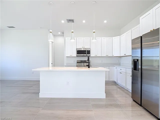 Kitchen with appliances with stainless steel finishes, decorative light fixtures, a center island with sink, white cabinets, and light stone countertops