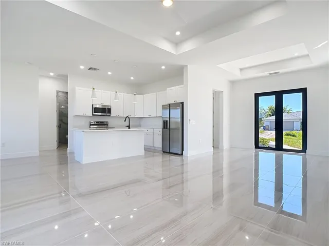Kitchen with open floor plan, a tray ceiling, light countertops, an island with sink, and appliances with stainless steel finishes