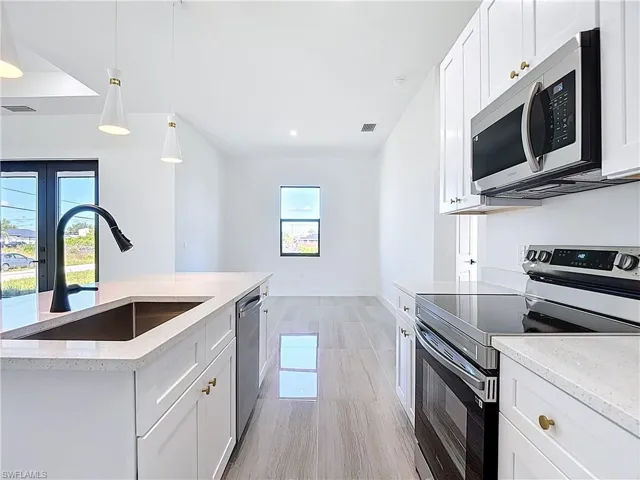 Kitchen featuring appliances with stainless steel finishes, white cabinets, pendant lighting, light stone counters, and recessed lighting