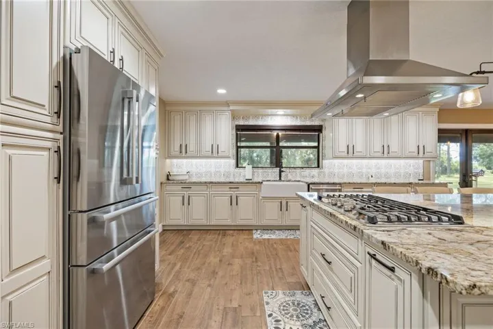 Kitchen with decorative backsplash, island exhaust hood, light stone countertops, cream cabinets, and recessed lighting