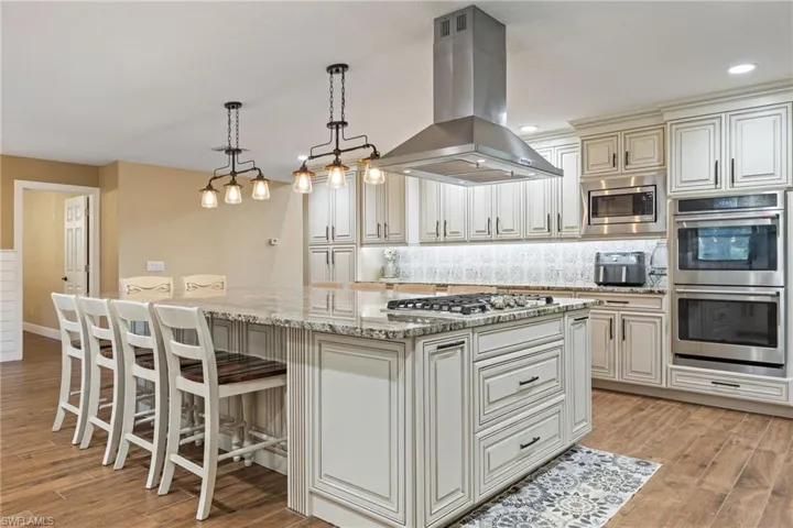 Kitchen featuring light stone counters, cream cabinetry, island range hood, backsplash, and recessed lighting