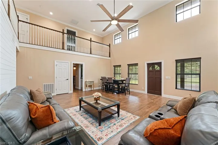 Living room featuring ornamental molding, wood finished floors, a towering ceiling, a ceiling fan, and recessed lighting
