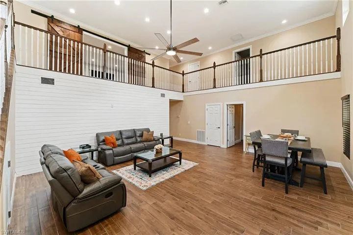 Living area with crown molding, a towering ceiling, wood finished floors, recessed lighting, and ceiling fan