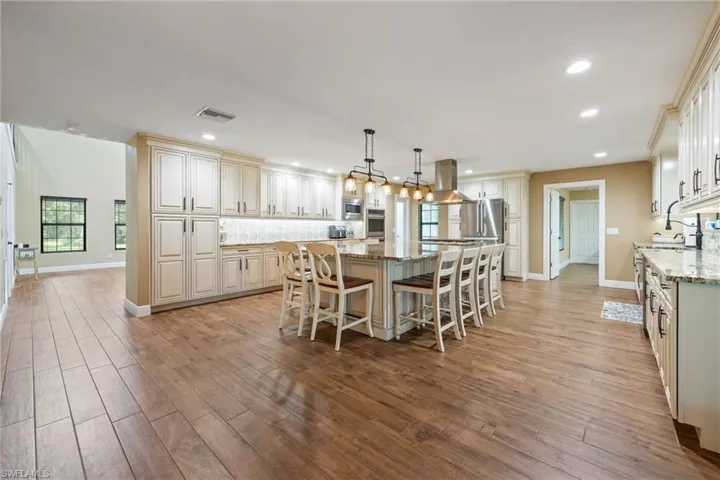 Kitchen featuring a oversized island, a kitchen island, tasteful backsplash, hanging light fixtures, and light stone countertops