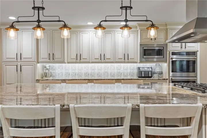 Kitchen featuring backsplash, wall chimney range hood, a kitchen breakfast bar, light stone counters, and recessed lighting