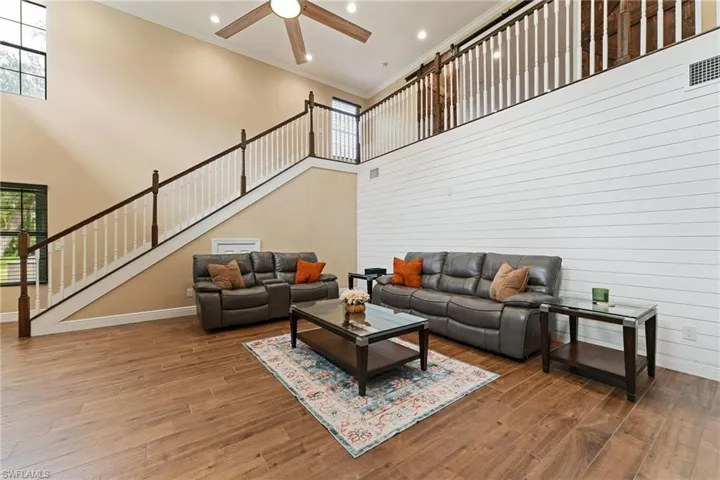 Living room with crown molding, stairway, a high ceiling, recessed lighting, and wood look floors