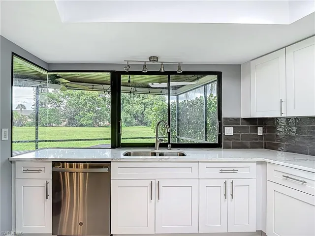 Kitchen with white cabinets, light stone countertops, stainless steel dishwasher, and tasteful backsplash
