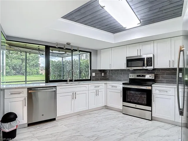 Kitchen featuring appliances with stainless steel finishes, light marble finish flooring, backsplash, and white cabinets