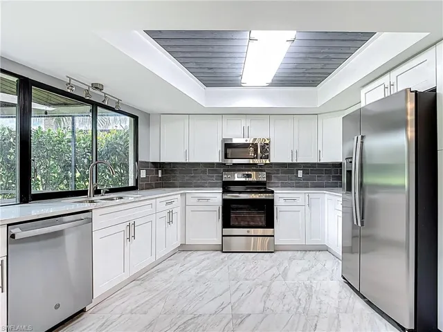 Kitchen with tasteful backsplash, appliances with stainless steel finishes, white cabinetry, and light stone counters