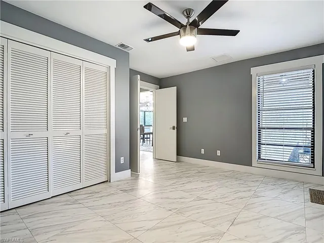 Unfurnished bedroom featuring light marble finish flooring, a ceiling fan, a closet, and multiple windows