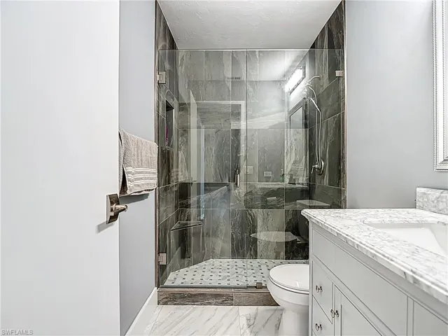 Full bathroom featuring a shower stall, vanity, light marble finish floors, and a textured ceiling