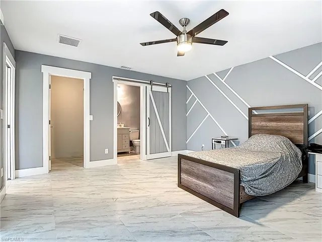 Bedroom featuring light marble finish floors, a barn door, a ceiling fan, and connected bathroom