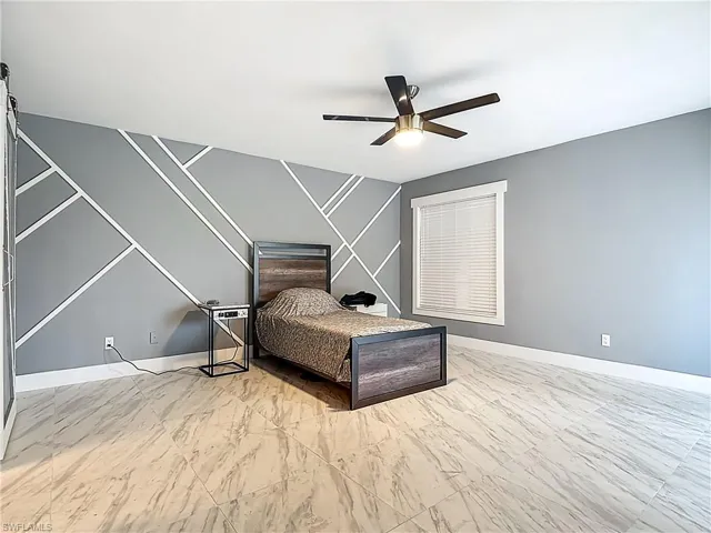 Bedroom featuring a ceiling fan, an accent wall, and light marble finish floors