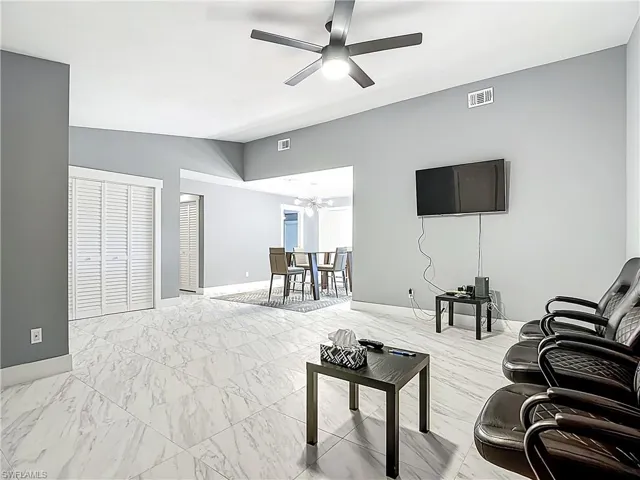 Living room with a ceiling fan, vaulted ceiling, and light marble finish flooring