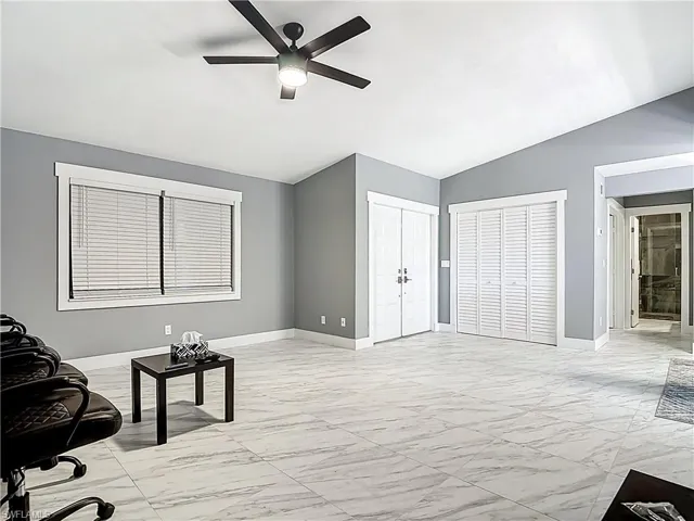 Living area featuring light marble finish flooring, vaulted ceiling, and ceiling fan