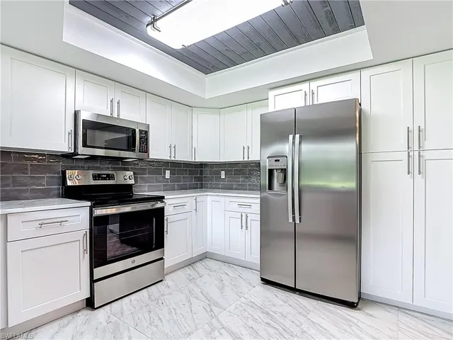 Kitchen with appliances with stainless steel finishes, white cabinetry, backsplash, light marble finish floors, and light stone counters