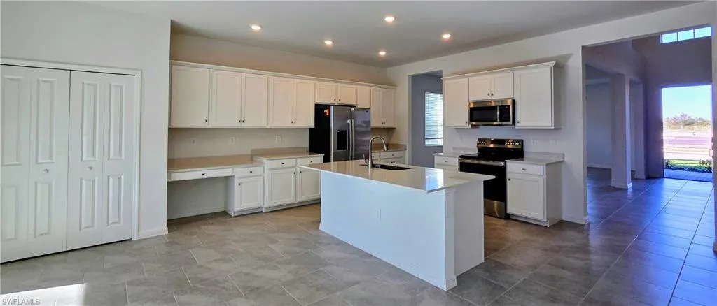 Kitchen with appliances with stainless steel finishes, white cabinetry, an island with sink, recessed lighting, and built in study area